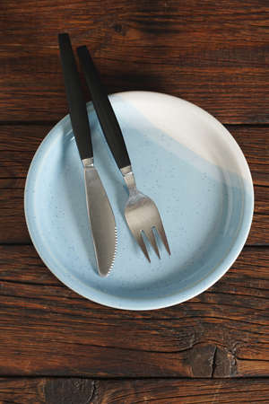 Empty clean plate with cutlery on dark wooden table, top view