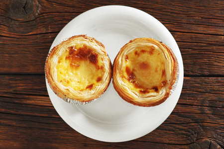 Directly above view of pastel de nata pastry on a plate on wooden background, top view