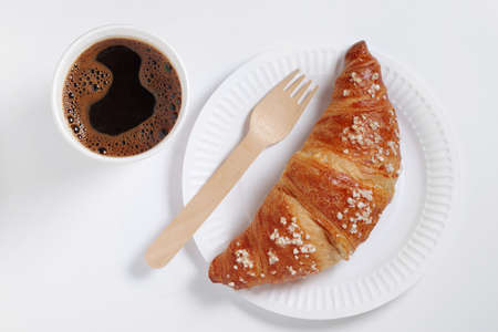 Croissant on paper plate and coffee cup on white background. Takeaway food. Biodegradable dishes