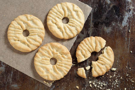 Round biscuit cookies whole and broken on old baking tray, view from above