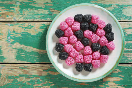 Jelly candies in the form of berries on a plate on old green wooden background, top view with copy spaceの写真素材