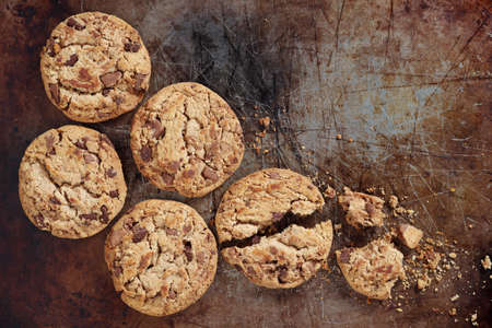 Chocolate chip cookies whole and broken on old baking tray, top view