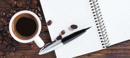 Notepad with pen and a cup of coffee on dark wooden background, top viewの写真素材