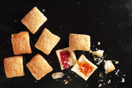 Puff pastry cookies with jam whole and broken on the background of an old black metal tray, top viewの写真素材