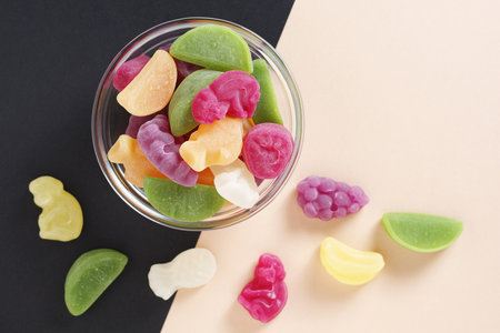 Mix of fruits gummy candies in glass bowl on two-color background, top viewの写真素材