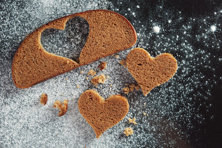 Heart-shaped slices of rye bread on background of black tray with flour, top view