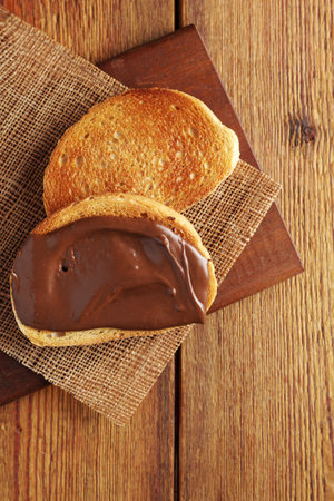 Fried white bread and one slice with chocolate hazelnut cream on wooden background, top view