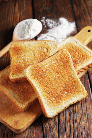 Slices of toasted bread on kitchen board on wooden table close up