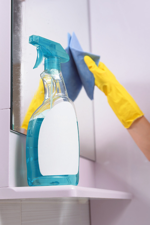 bottle of window cleaner for windows and mirrors stands on a shelf near the mirror. Hand in rubber glove with a rag.の写真素材