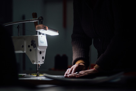 Sewing machine in dark with working hands on backdropの写真素材