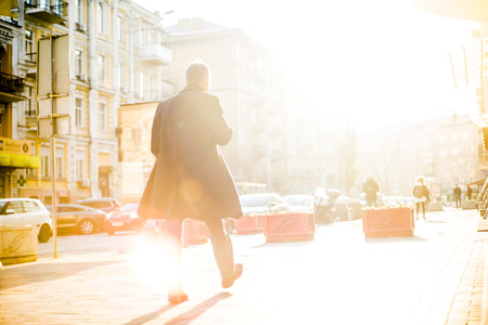 People with unrecognizable faces are walking through the streets fully shined by evening warmの写真素材
