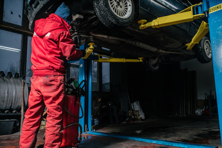 Young caucasian man in red work clothing repairing car with professional toolsの写真素材