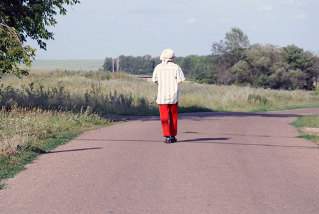 A woman is walking along a country road in red trousers against a backdrop of a landscapeの写真素材