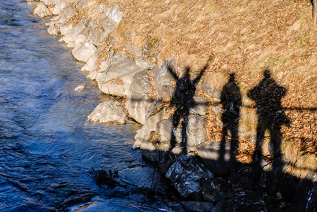 Three shadows of men, standing on the bridge, reflex in the riverbank of a dark blue river. One of the men put his hands up - it is expression of joy and happiness.の写真素材