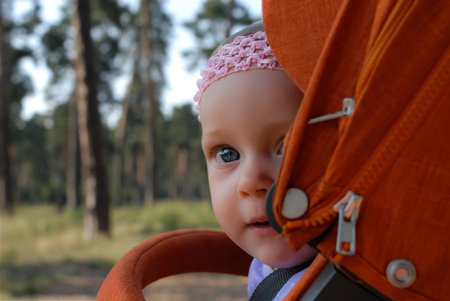 A close-up of a nine-month baby girl looking curiously with her clear blue eyes and sitting in an...