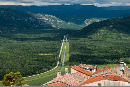 A view of the long road leading from the town with red tiled roofs far away to the horizon with green hills, Photo was shot in Motovun, Croatia. Concept - a road to somewhere; a beginning of a journeyの写真素材
