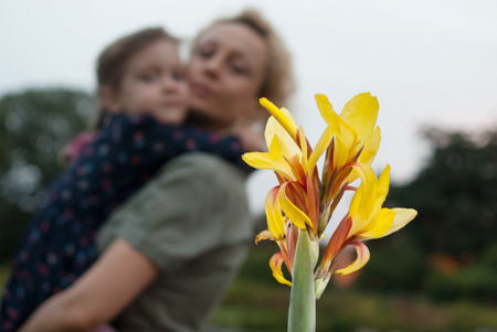 Woman with a little girl in her hands look at a blooming yellow gladiolus flower. Blurred effect. Concept - happy motherhood, happy childhood.の写真素材