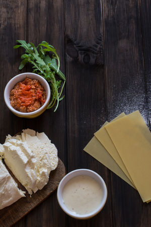 Process of preparing lasagna. Traditional italian food. Raw lasagna dough, mozarella cheese, bolognese sauce, bechamel sauce, arugula on wooden background.の写真素材