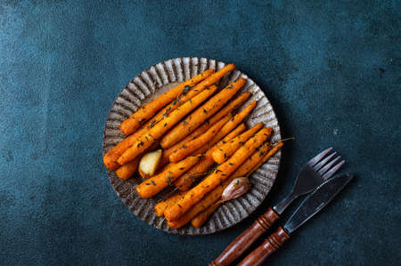 Roasted Carrots Ready to Eat. Glazed carrot with herbs and garlic top view. Fried carrot on dark background. Sauteed vegetables. Comfort food. Sustainable consumption.の写真素材