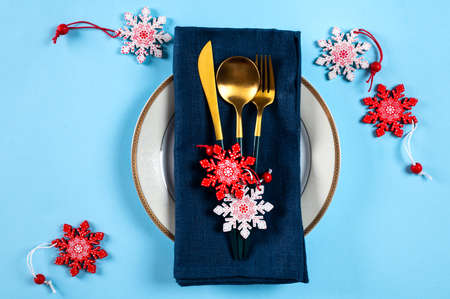 Christmas table setting with modern dishware and decorations on blue background. Top view. New Year...