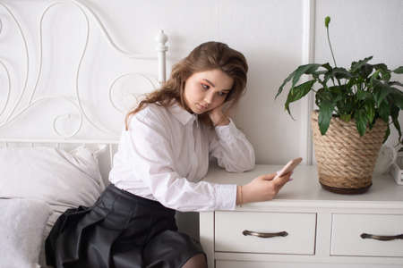 A happy beautiful business consultant woman in formal attire, using a mobile phone, reading the news or sending text messages, sitting in a room with a bed, enjoying a busy working dayの写真素材