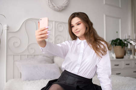 A happy beautiful business consultant woman in formal attire, using a mobile phone, reading the news or sending text messages, sitting in a room with a bed, enjoying a busy working dayの写真素材
