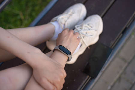 The girl is sitting on a bench, laughing and looking at the phone, there is a laptop nearby.の写真素材