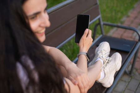 the girl is sitting in a cafe at the bar, looking at the phone, holding glasses in her hand, a lapto.の写真素材