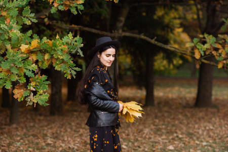 short dress, autumn weather, hat with brim, black jacket, happy girl, smile, yellow leaves, autumn treesの写真素材