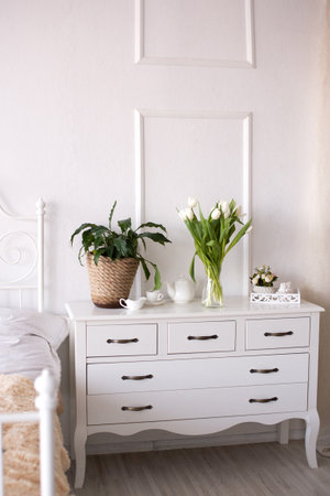 White tulips and a green indoor flower stand on the bedside table next to tea dishesの写真素材