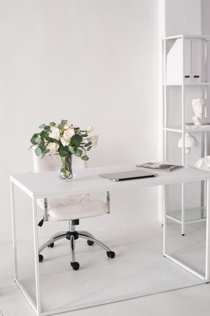 Office environment. A white room with a desk on which there is a vase, a laptop and magazinesの写真素材