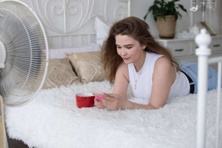 A happy beautiful business consultant woman in formal attire, using a mobile phone, reading the news or sending text messages, sitting in a room with a bed, enjoying a busy working dayの写真素材