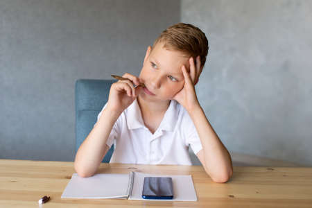 Cute boy writes in an open notebook and looks at the phone.の写真素材