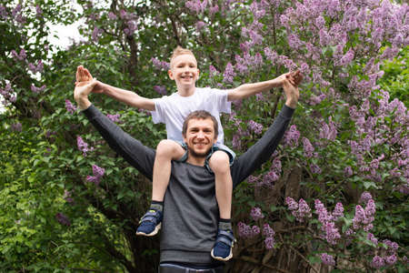 dad holds his son, son raised his hands, family in nature, dad walks with his son, green trees, sit on his shoulders, cute child, exemplary fatherの写真素材