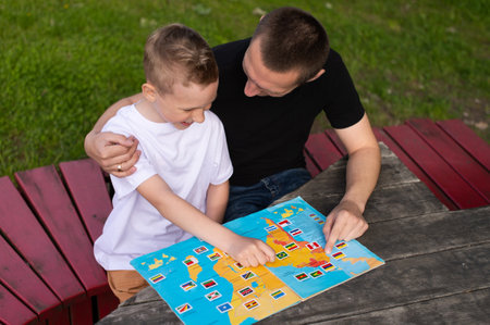 flipping through a book, showing an album, hugging your son, white T-shirt, black T-shirt, sitting next to two people, relaxing in the park, planning a trip, studying geographyの写真素材