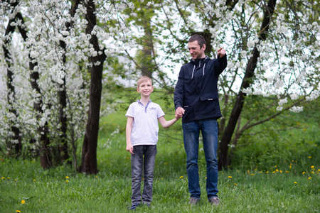 standing next to the child, teaching the son, showing the direction, entertaining the child, studying, dad, son, child, father, upbringing, development, interest, watching, playing, family vacation, nature walk, spring, reaching for flowers, blooming treeの写真素材
