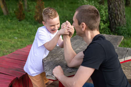 show hands, powerlifting, measure strength, play with dad, family weekend, white t-shirt, blonde hair, sit on a bench, play in the parkの写真素材