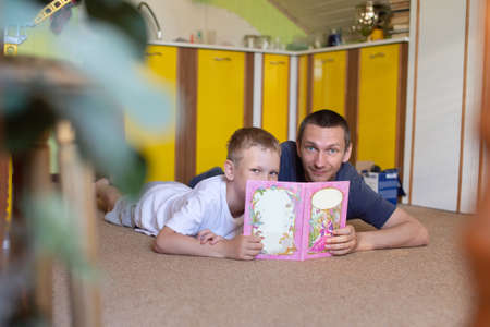 father and son, boy with dad, spending time, talking with dad, reading a book, watching cartoons, flipping through a book, gadget, lying on the floor, playing at home, time with dadの写真素材