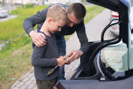 Cute boy helps Dad fix the car. Unscrew the wheelの写真素材