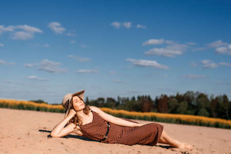 A young girl in a dress and with a hat is lying on the sand.の写真素材