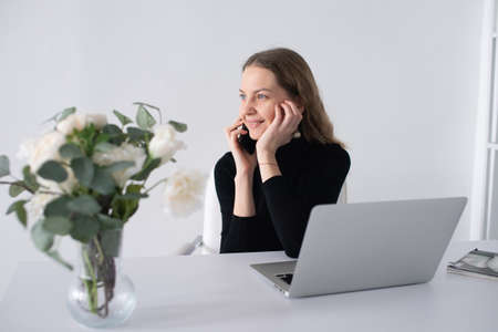 The girl works in a white office with a laptop and flowers on the table.の写真素材