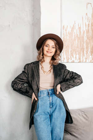 hands on the belt, brown hat, dark jacket, man in the room, makeup, big chain, gold chain, stylist, girl standing, looking at the cameraの写真素材