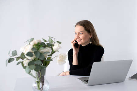 The girl works in a white office with a laptop and flowers on the tableの写真素材
