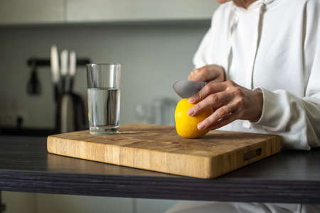 With a knife, cut a yellow ripe lemon for water in a glassの写真素材