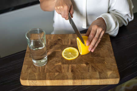 With a knife, cut a yellow ripe lemon for water in a glassの写真素材