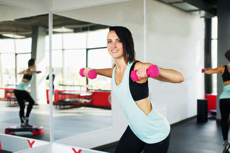 fitness trainer spreads his arms with dumbbells to the sidesの写真素材