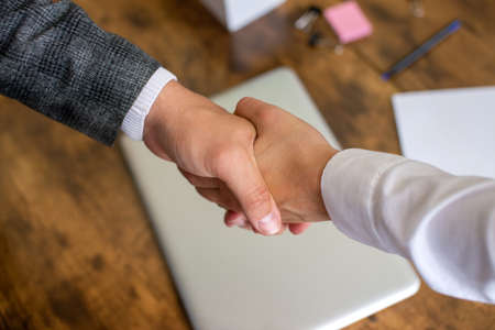 Shake hands near laptop and desktop, working relationshipの写真素材