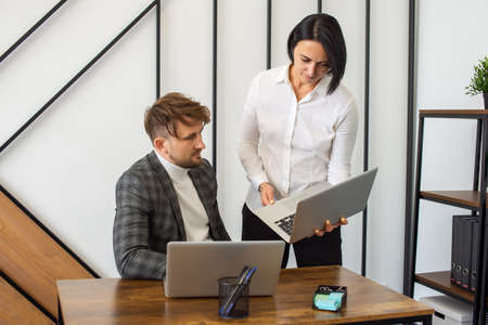 A man looks at a laptop to a woman in the office