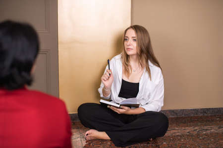 A nice psychologist girl sitting on the floor listens attentively to the clientの写真素材