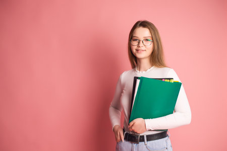 Cute student girl with glasses holds folders on pink background.の写真素材